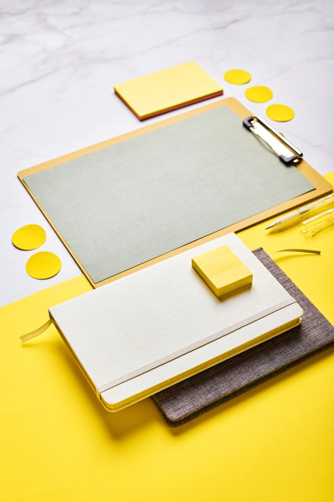 Material de oficina como libretas, notas adhesivas y un portapapeles sobre un fondo amarillo.